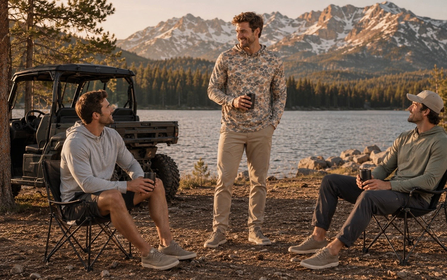 Three men wearing Hudson Bros. performance apparel, including the Everyday Shade Oxbow Hoodie in Camo, relax beside a mountain lake at golden hour.